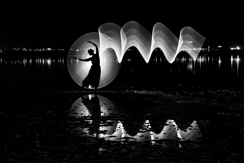 Silhouette einer Frau, die im Freien auf einem See tanzt, mit Lichtmalerei und Reflexionen auf dem Wasser